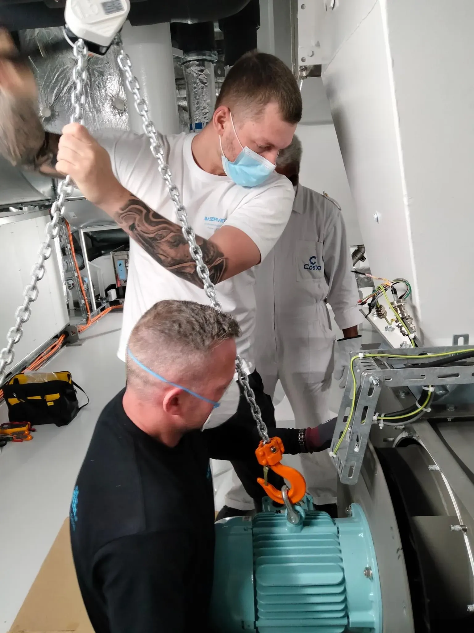 To teknikere løfter en ventilatormotor med en kædetalje